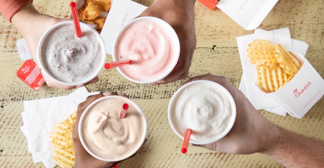 Four hands holding Chick-fil-A milkshakes with Waffle Fries in the background