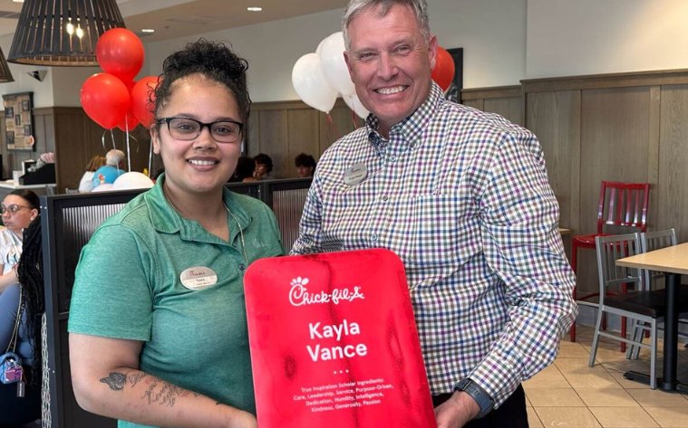 A Team Member and an Owner-Operator standing together inside a Chick-fil-A Restaurant holding a large sauce packet