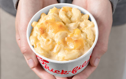 A person holding a paper bowl of Mac & Cheese